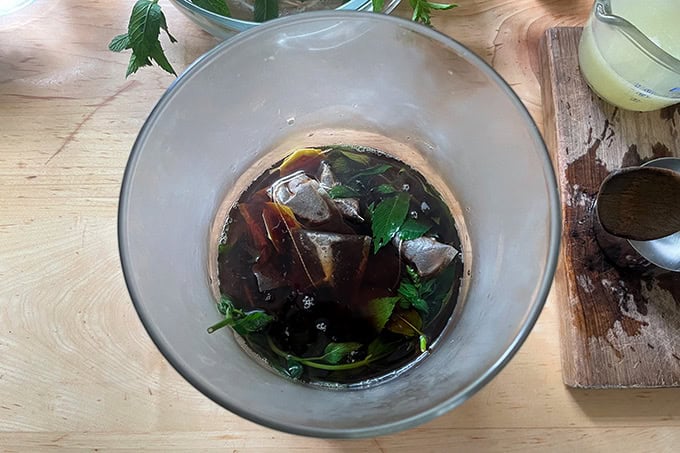 A glass vessel holding tea bags steeping in hot water and mint.