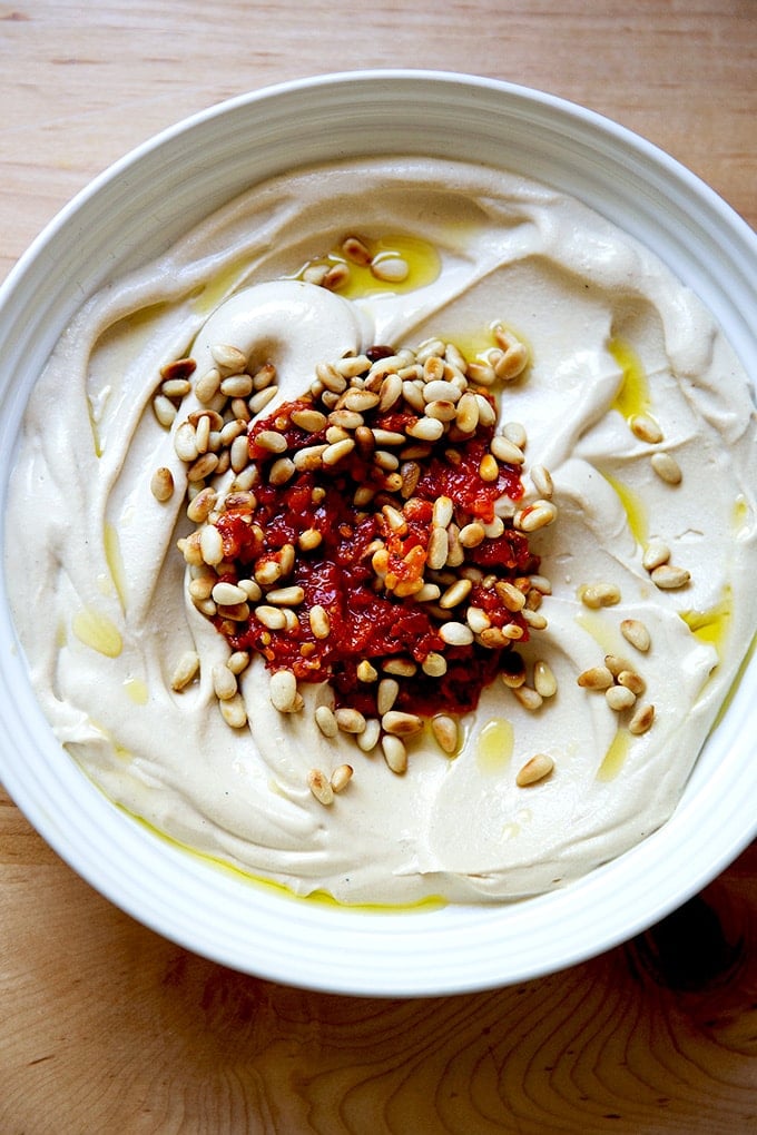 A bowl of creamy hummus with chili paste and pine nuts.