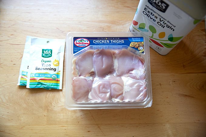 A package of chicken thighs aside two packets of taco seasoning and a large tin of oil.
