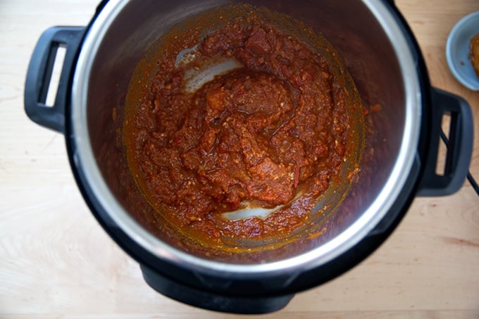 An Instant Pot filled with tomatoes, ginger, garlic, salt, and curry powder.
