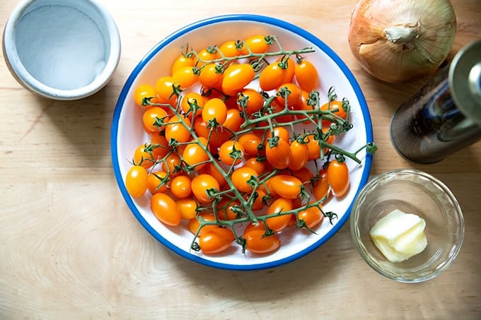 A plate of sun gold tomatoes aside salt, butter, olive oil, and an onion.