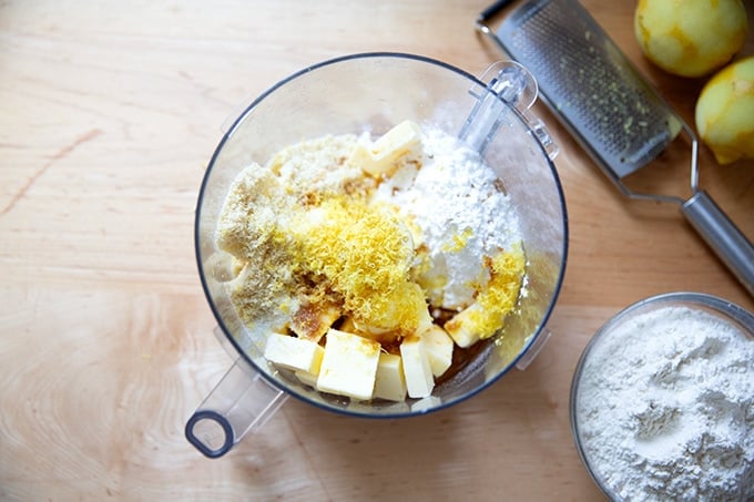 A food processor filled with the ingredients to make lemon-almond snowball cookie dough, not yet blended. 