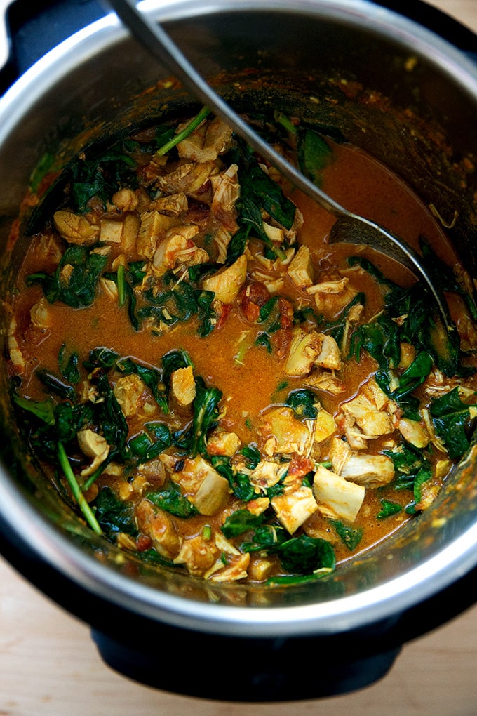 An Instant Pot filled with butter chicken and wilted spinach.