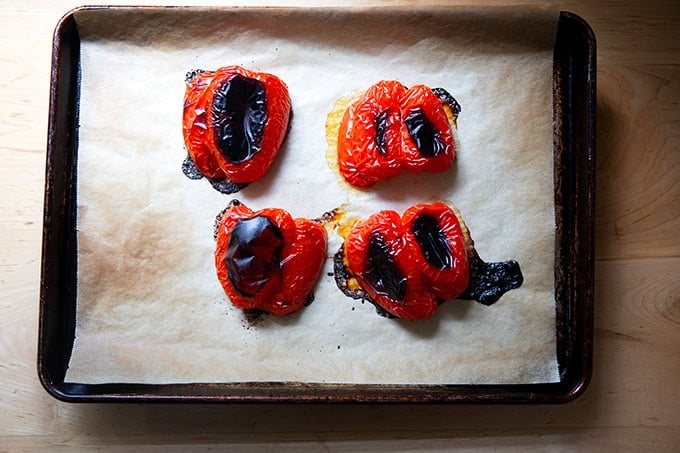 A sheet pan topped with 4 halved roasted red peppers. - 4