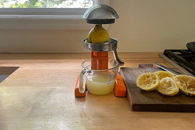 A juicer with a lemon and a liquid measure filled with fresh lemon juice.