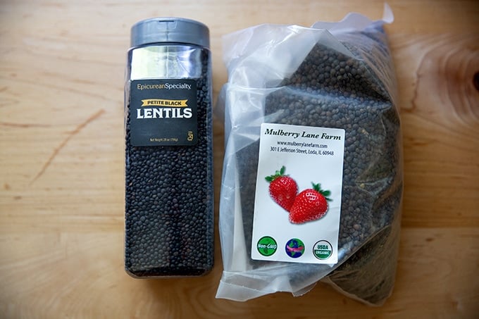 Black lentils in a tub aside a bag of French green lentils.