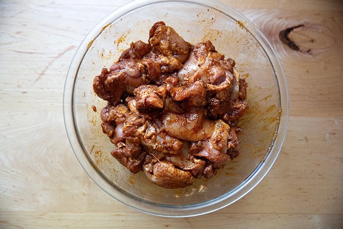 A bowl of chicken thighs marinating in olive oil and taco seasoning.