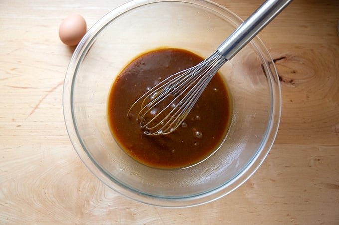 A bowl of whisked together sugars, butter, and molasses aside an egg.