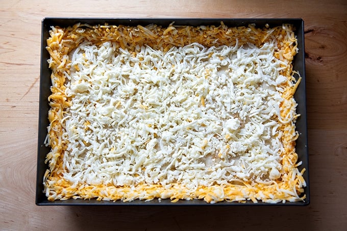 A Detroit-style pizza, unbaked, with cheese at the edges and center.