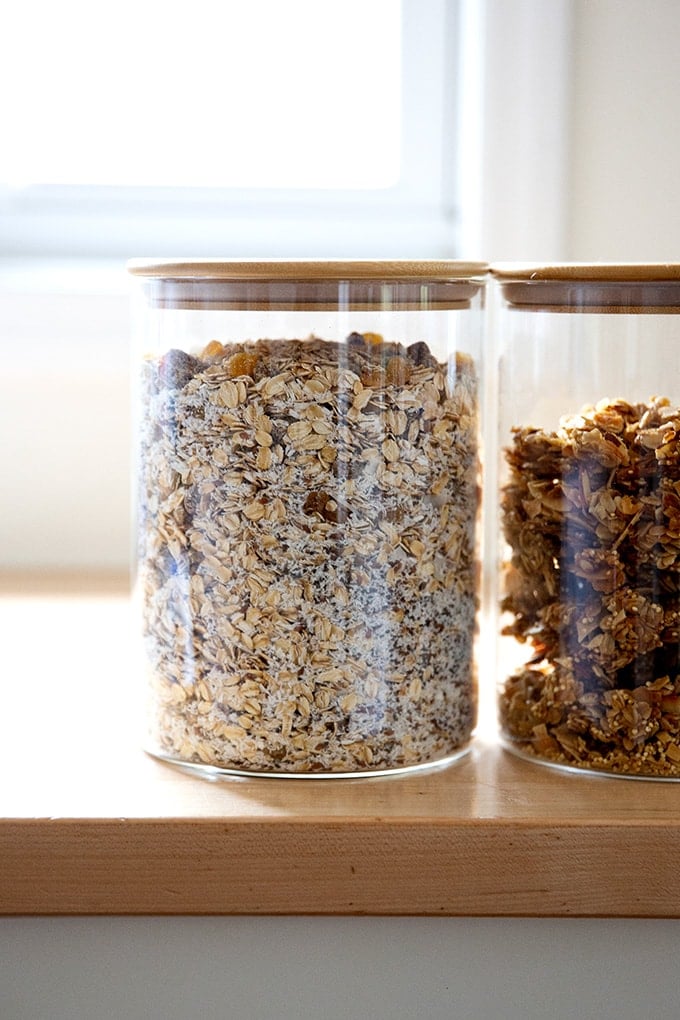 Two containers filled with muesli and granola on a countertop.