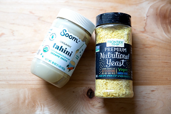 A jar of tahini and a tub of nutritional yeast on the countertop.