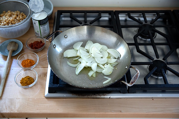 A large skillet stovetop holding onions and oil.