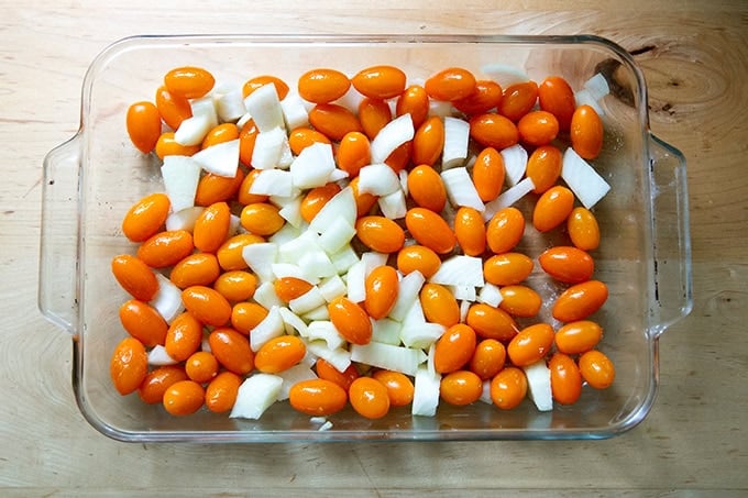 A 9x13-inch pan filled with yellow cherry tomatoes and onions, tossed together with olive oil and salt.