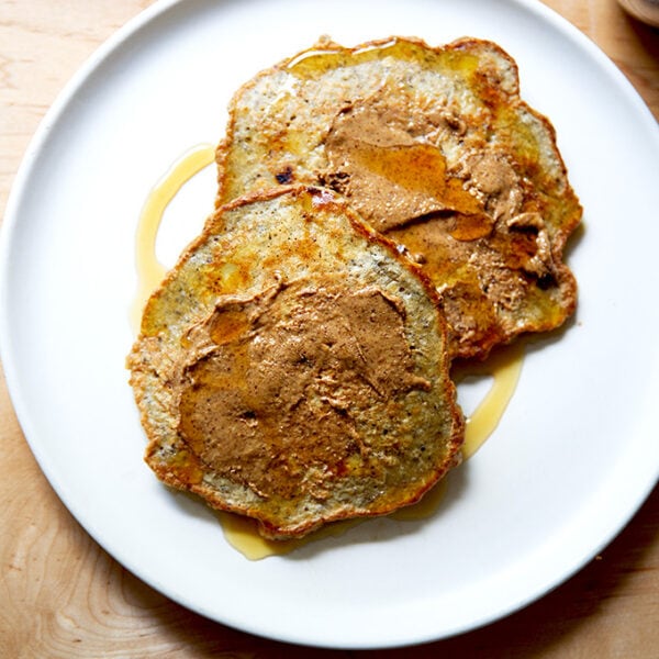 Banana-oat pancakes on a plate with almond butter and maple syrup.