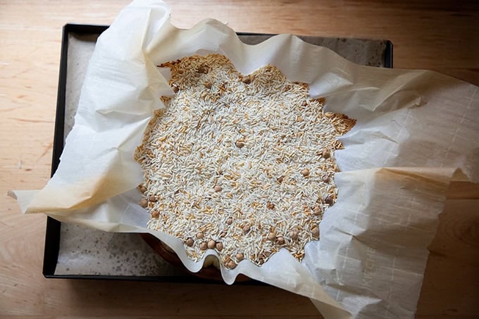 An overhead shot of pie weights — a mix of dried rice and chickpeas — filling a parchment-lined pie plate. - 12