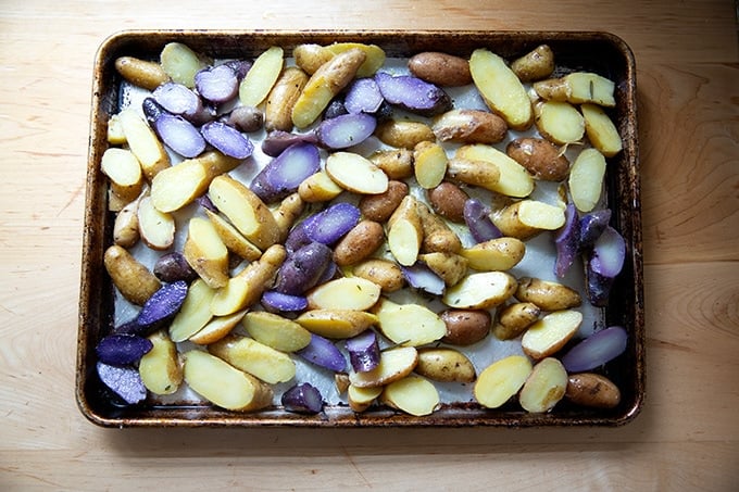 A sheet pan of fingerling potatoes dressed with olive oil and salt ready for the oven.