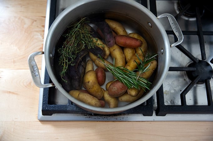 A pot on the stovetop filled with water, herbs, salt, and fingerling potatoes.