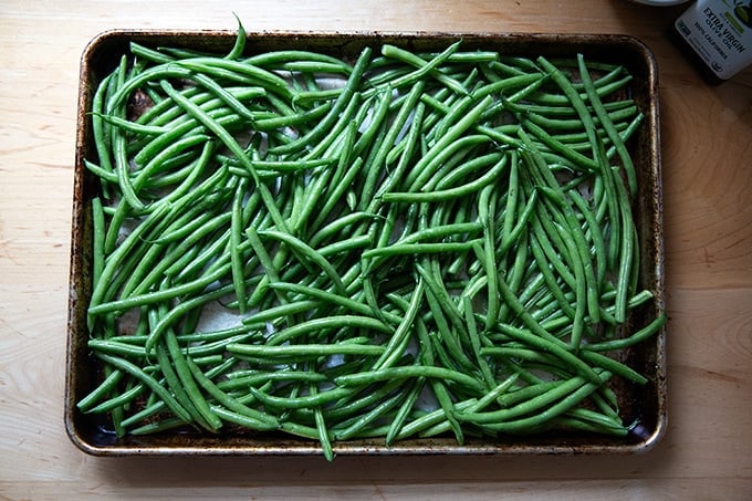 A sheet pan filled with green beans tossed wit olive oil and kosher salt.