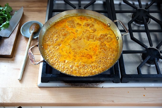 A skillet on the stovetop holding the makings of curried Thai chickpeas.