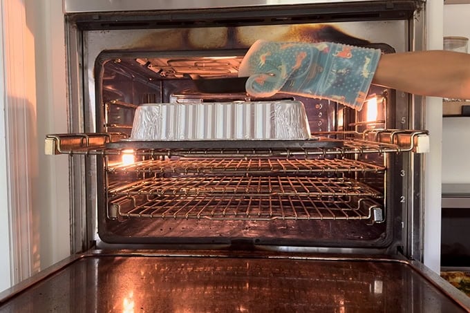 Removing a weight from an aluminum pan on a baking steel in an oven.