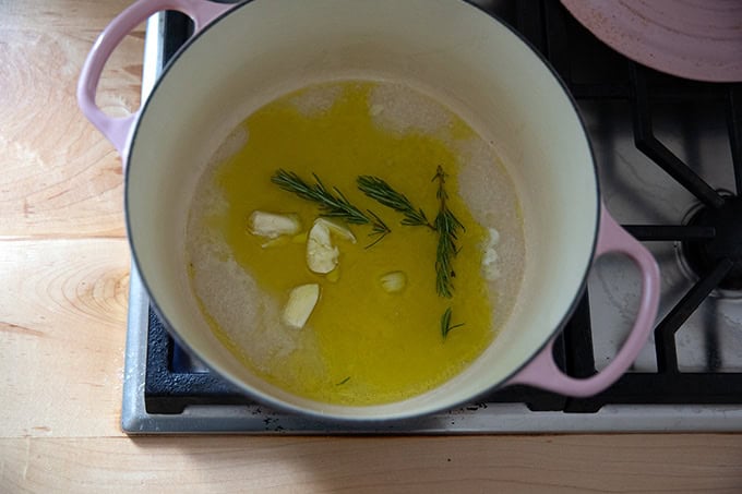 A large pot on the stovetop filled with a little bit of olive oil, water, rosemary sprigs, and garlic. - 4