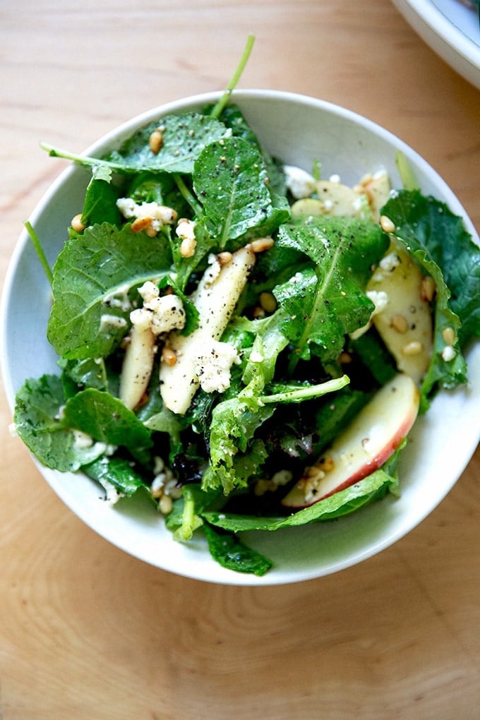 A fall salad of greens, pine nuts, goat cheese, and apples in a bowl.