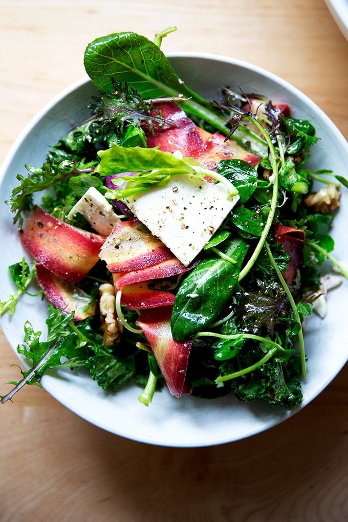 A spring salad in a bowl: greens, radishes, carrots, feta, and walnuts.