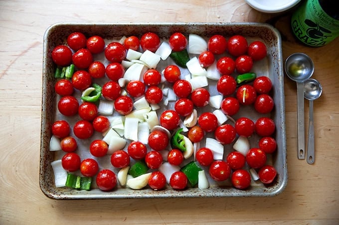 Tomatoes, garlic, chopped onions, and jalapeños on a small sheet pan tossed with olive oil and kosher salt. - 3