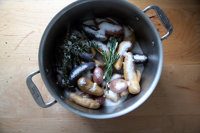 A pot of water filled with fingerling potatoes covered with salt and herbs.