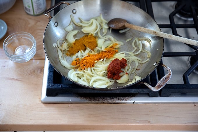 A skillet stovetop with sautéd onions, turmeric, curry powder, and Thai red curry paste.