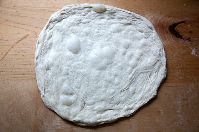 A round of pizza dough stretched out on a counter top.
