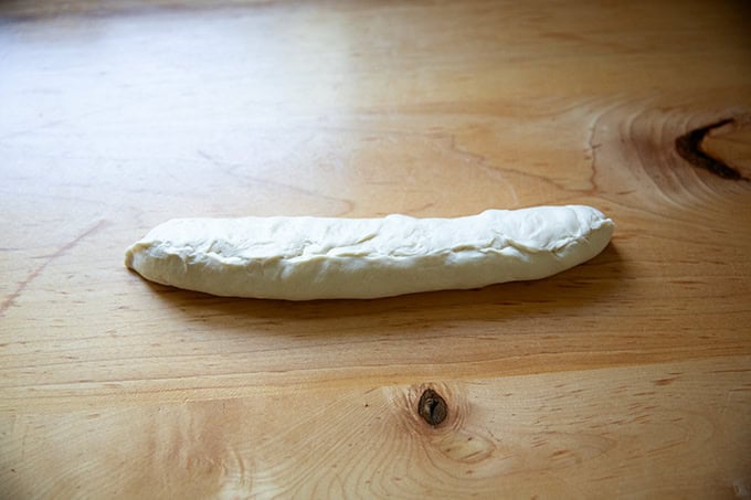 Final step of shaping a baguette, with the seem pinched together and facing up.