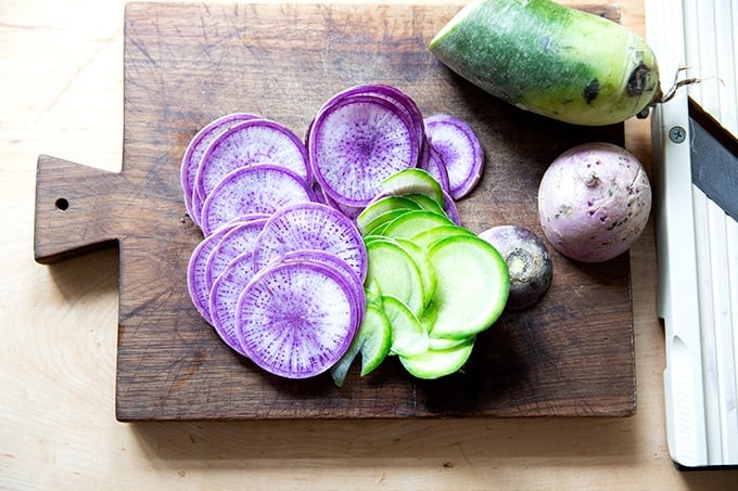 Thinly shaved radishes on a board.