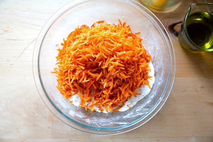 Shredded carrots in a bowl of dry ingredients to make carrot cake.