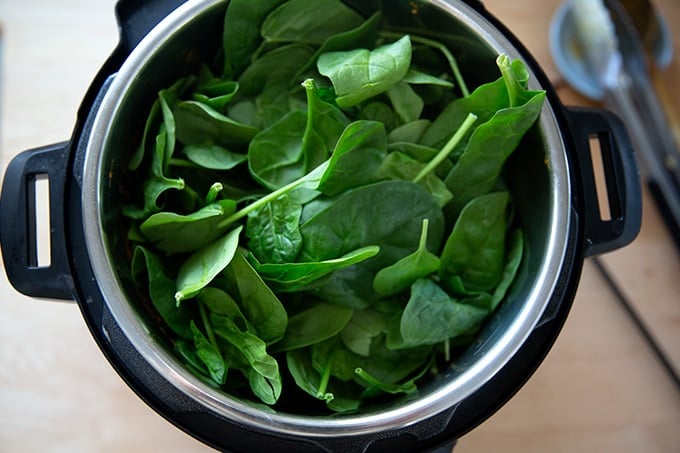 An Instant Pot filled with butter chicken and a heap of spinach.