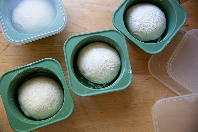 Four rounds of baguette dough in individual storage containers.