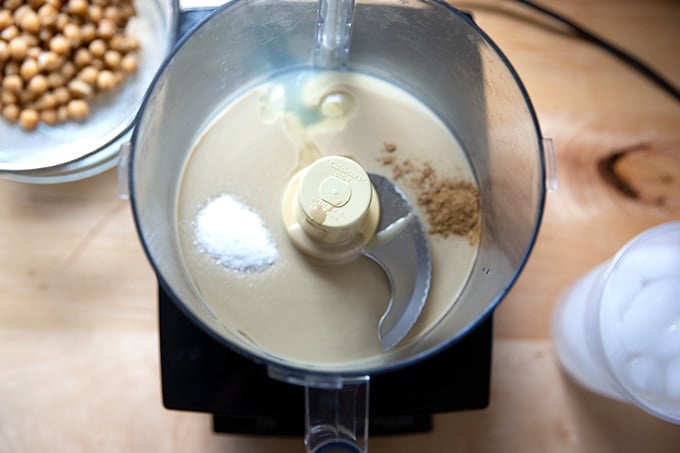 A food processor holding tahini, salt, cumin, garlic, and lemon juice.