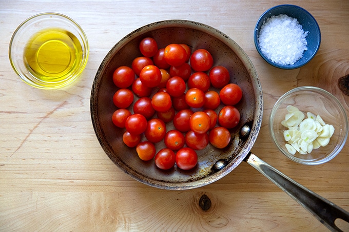 A pint of cherry tomatoes in a skillet aside olive oil, garlic, and salt.