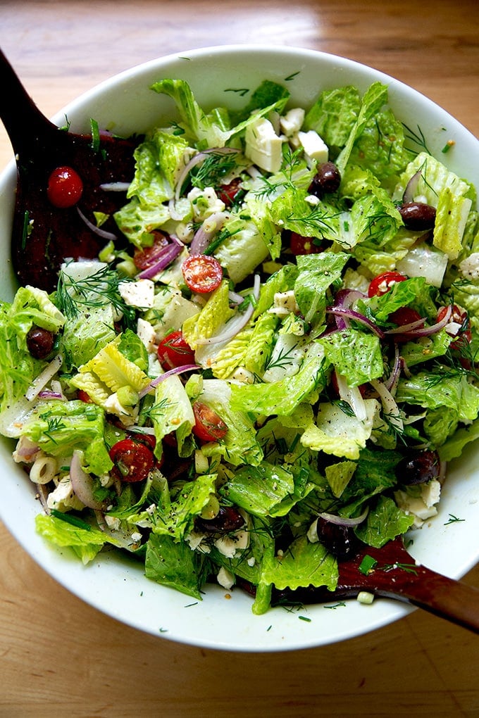 A tossed Greek salad in a large white bowl.