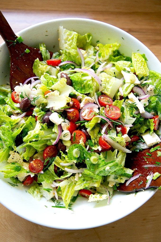 A tossed Greek salad in a large white bowl.