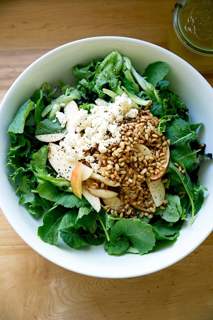 A salad of greens, pine nuts, apples, and goat cheese in a bowl.