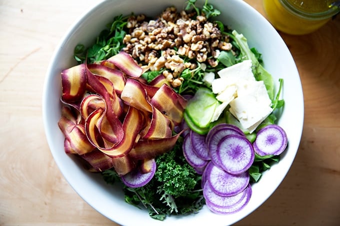 An untossed spring salad with greens, radishes, carrots, feta, and walnuts.