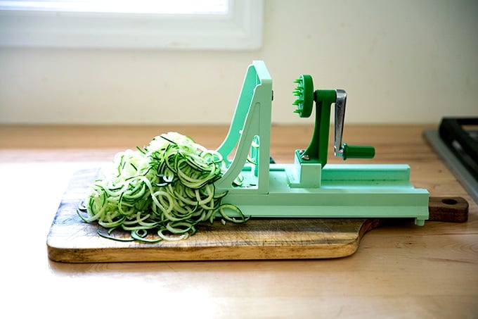 A turning slicer slicing a cucumber on a countertop. 