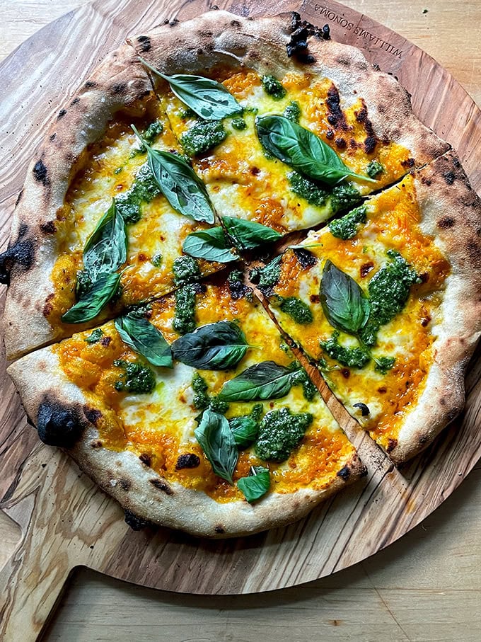 A pizza topped with yellow tomato sauce, basil pesto, and basil. 