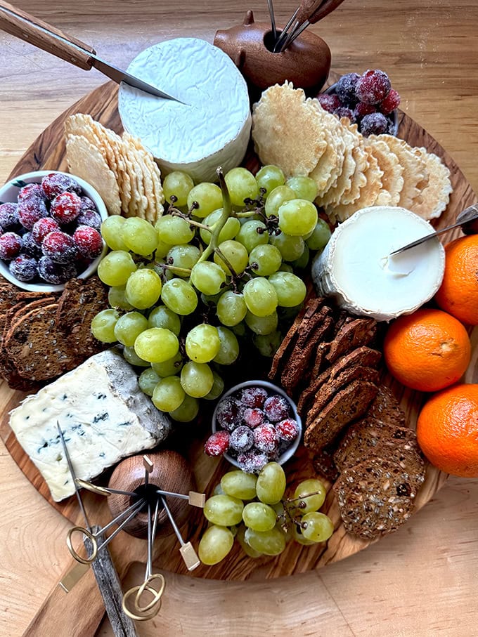 A cheese board loaded with cheese, crackers, grapes, and sugared cranberries. 