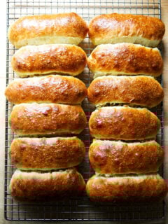 Twelve just-baked brioche hot dog buns on a cooling rack.