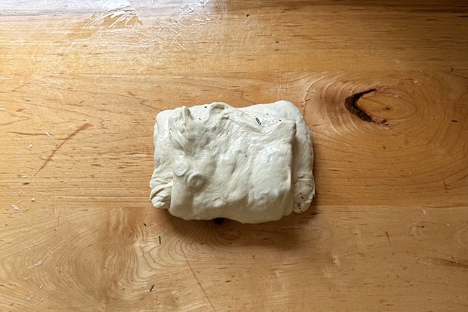 Final fold of a batch of rosemary-olive sourdough on a counter top. - 33