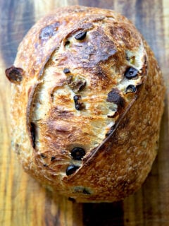 A freshly baked loaf of rosemary-olive sourdough bread on a wooden cutting board.