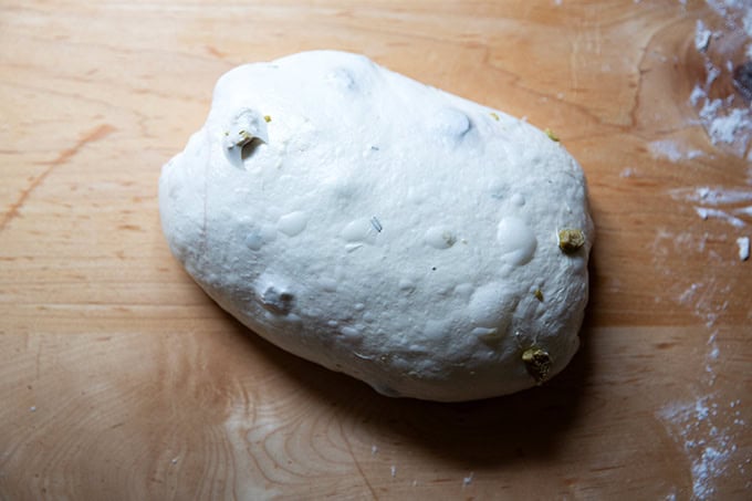 An unbaked loaf of rosemary-olive sourdough shaped into a batard. - 41