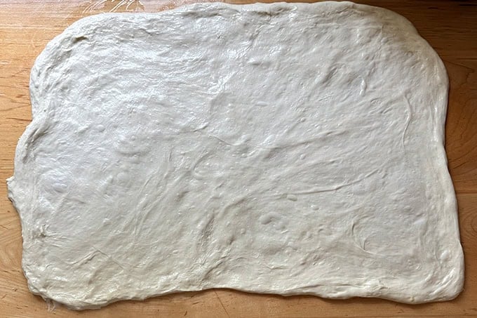 Sourdough dough stretched thinly across a counter top into a 20x15-inch rectangle. - 29